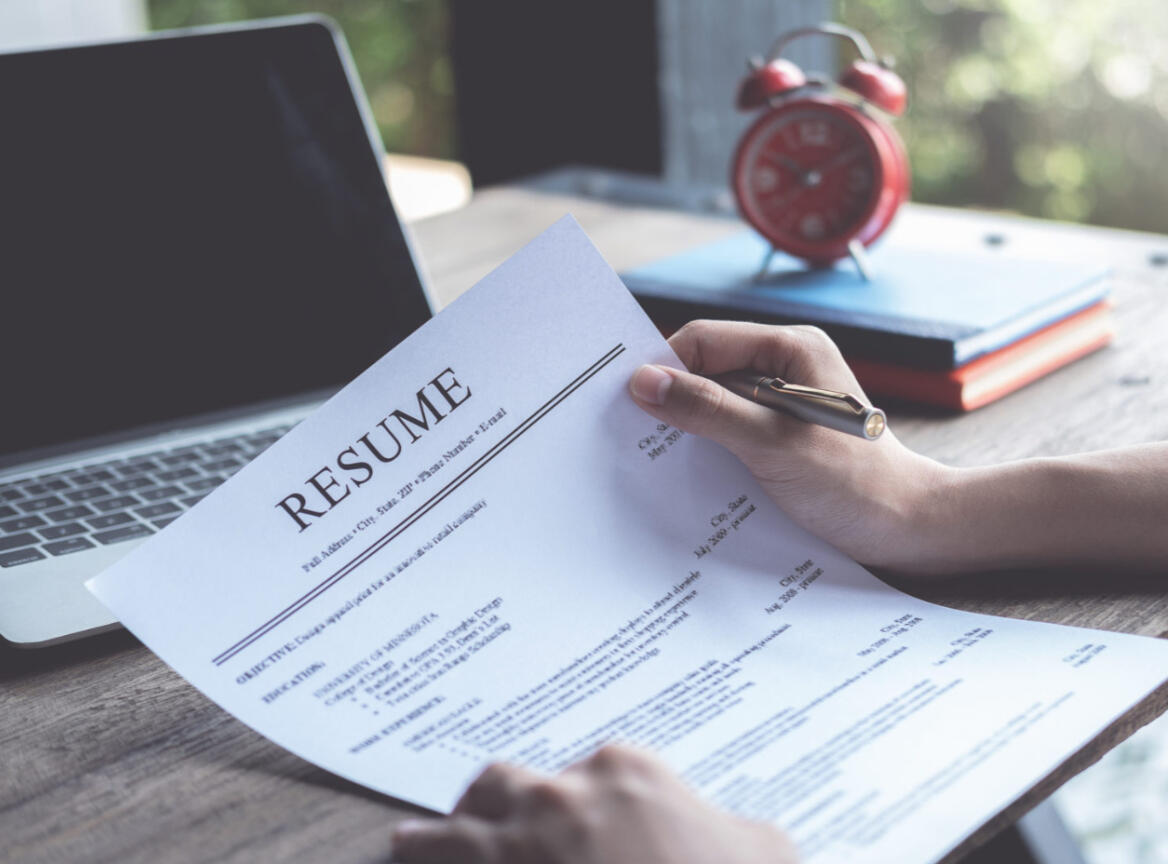 Hands holding a resume in front of a computer